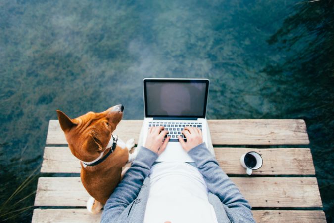Man with coffee, dog and laptop sitting on the lake