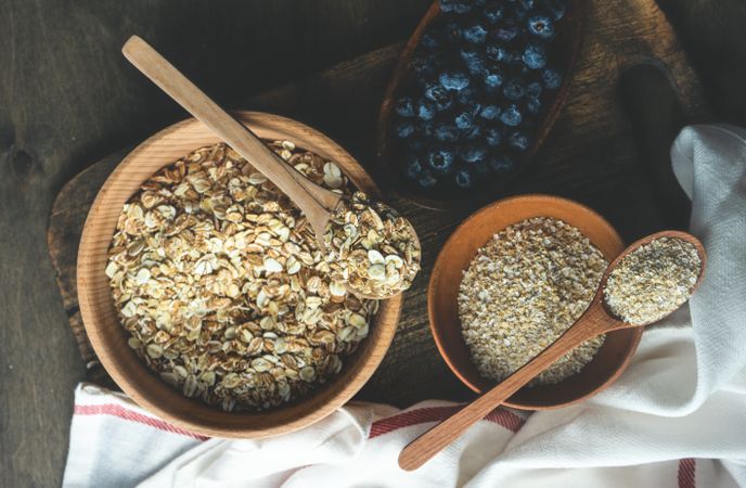 Wooden bowls of dry oats with blueberries on kitchen counter