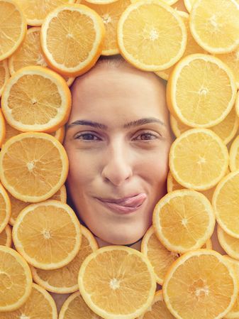 Young woman licking lips among slices of oranges