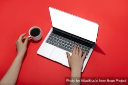 Top view of person typing on laptop keyboard on red table with coffee bxJwv5