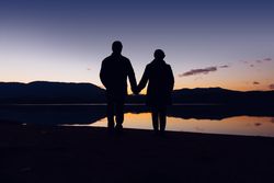Anonymous couple standing near water during sunset