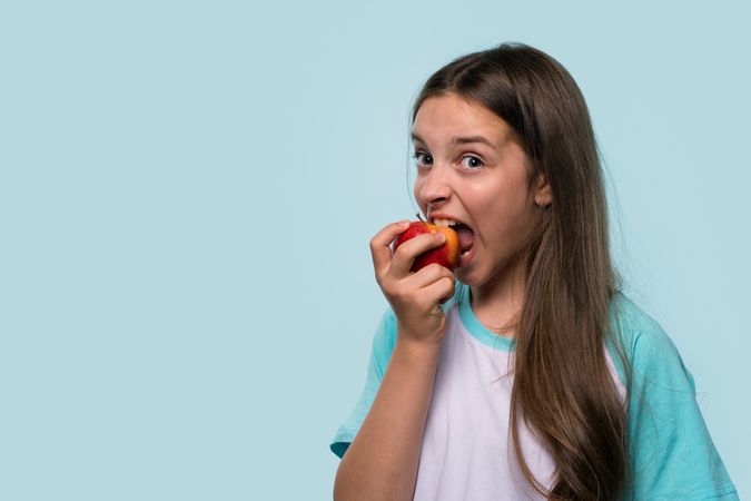 Girl takes big bite of red apple