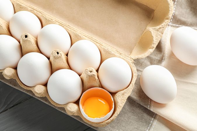 chicken eggs in carton box and kitchen towel on wooden table, space for text and top view
