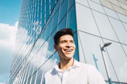 Smiling young man in sunlight under skyscraper