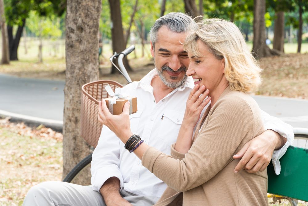 Smiling man gives a box to woman at park