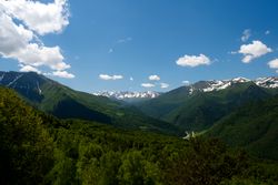 Snow-capped mountains and lush green valleys under blue sky.