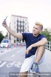 Young blonde man sitting outside and taking a selfie bE9Q61