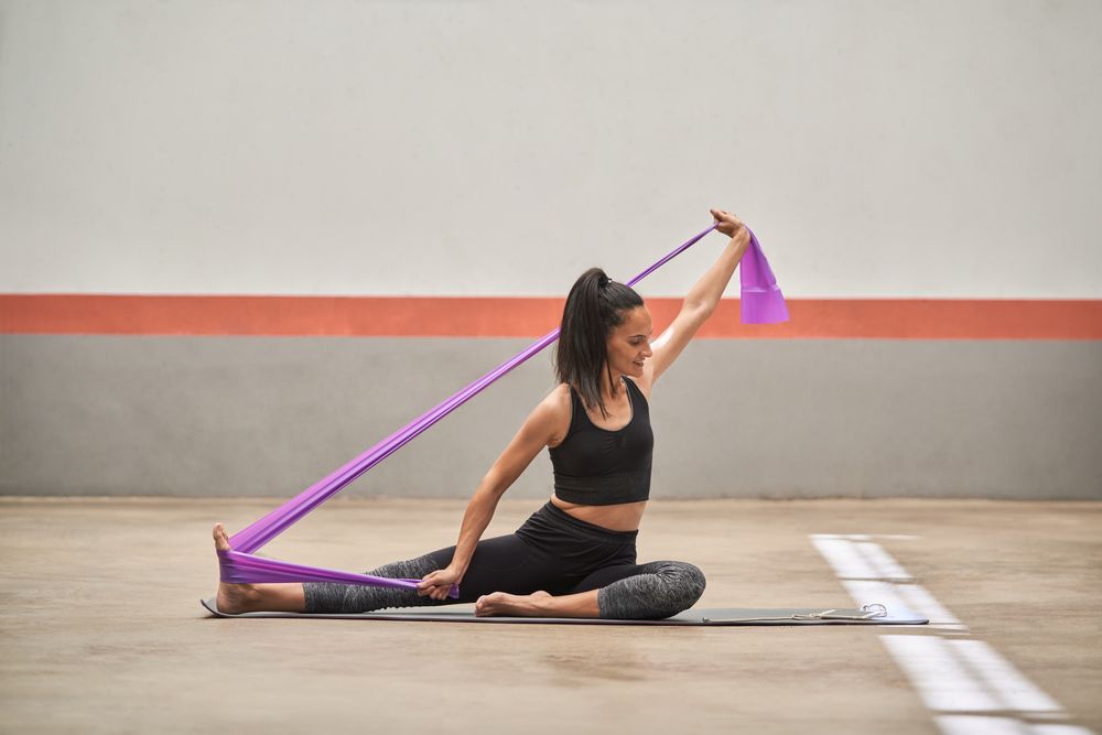 Adult sportswoman stretching body with resistance band