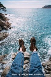 Hiker sitting on rocks overlooking ocean in leather boots, vertical bD8WQb
