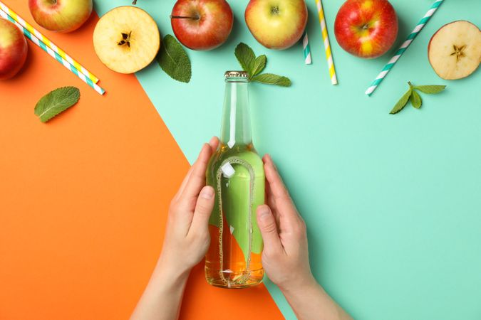 Female hands hold bottle of cider on two tone background. Composition with cider
