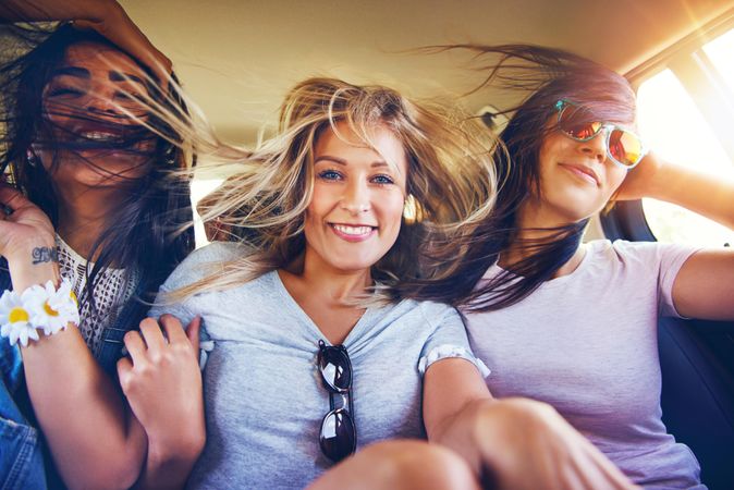 Group of happy female friends laughing with each other while riding in back of vehicle