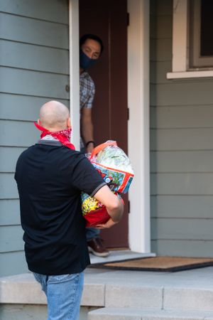 Back view of a man bringing groceries to his neighbor at his house