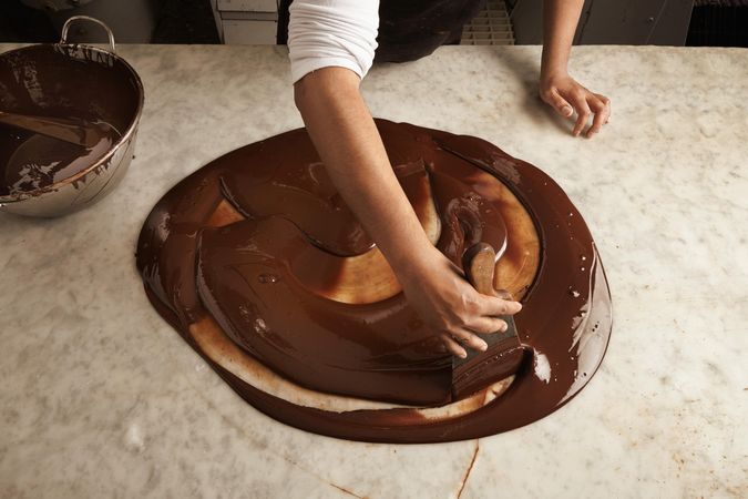 Top view of chef working with melted chocolate on marble counter