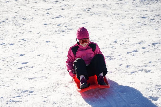 Child in pink snow suit sitting on sled