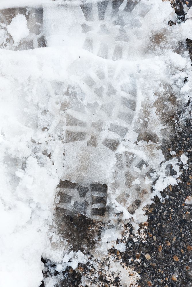 Shoe prints on wet snow on asphalt road