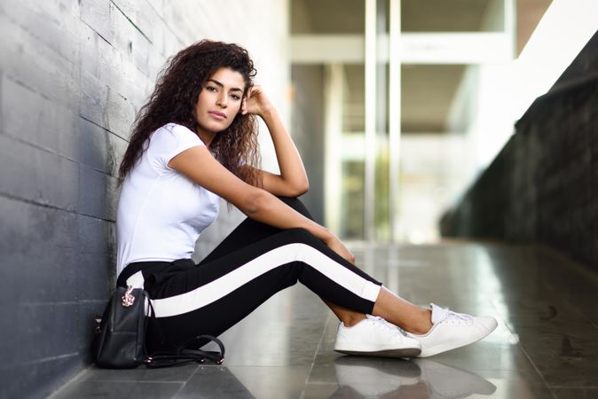 Serious female in leggings sitting outside of building entrance