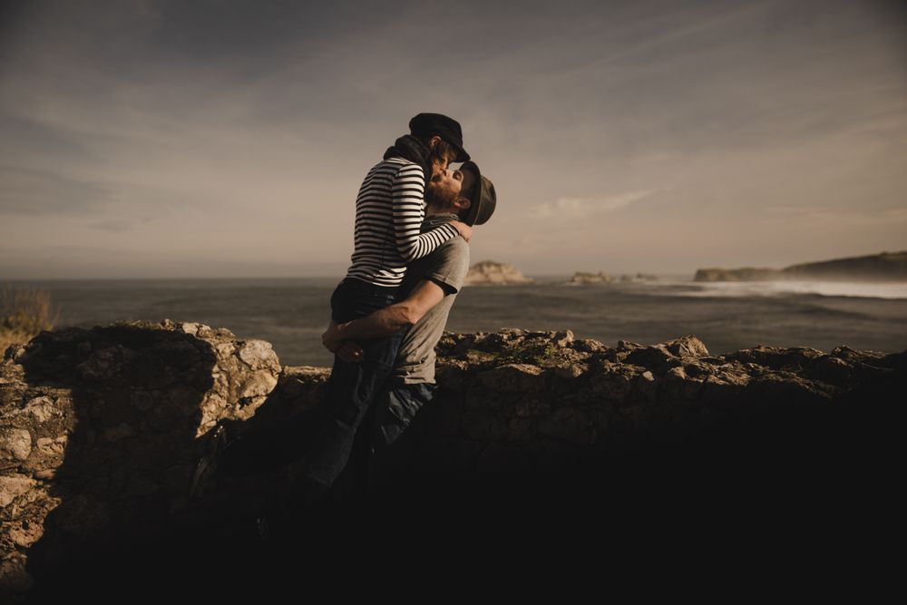 Man kissing and holding woman on hands near stones on shore