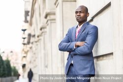 Serious male in business attire leaning on wall with arms closed, copy space bxBzB5
