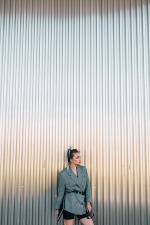 Woman with tablet in stylish suit standing nearby wall holding sunglasses