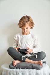 Focused preteen boy operating remote controller sitting on pillo