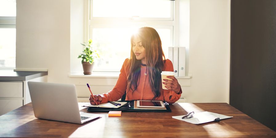 Businesswoman working at her desk with to-go coffee in hand