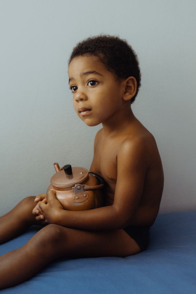 kid sitting in cozy room with tea pot looking away