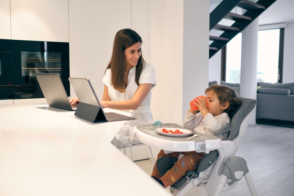 Glad mom using laptop while child having breakfast at home