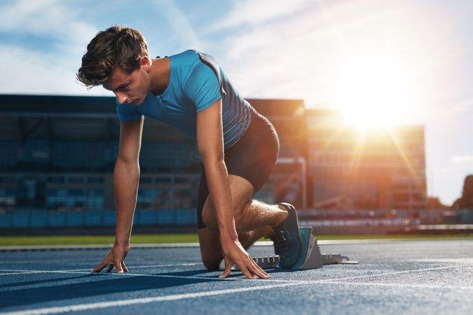 Young male athlete at starting block on running track