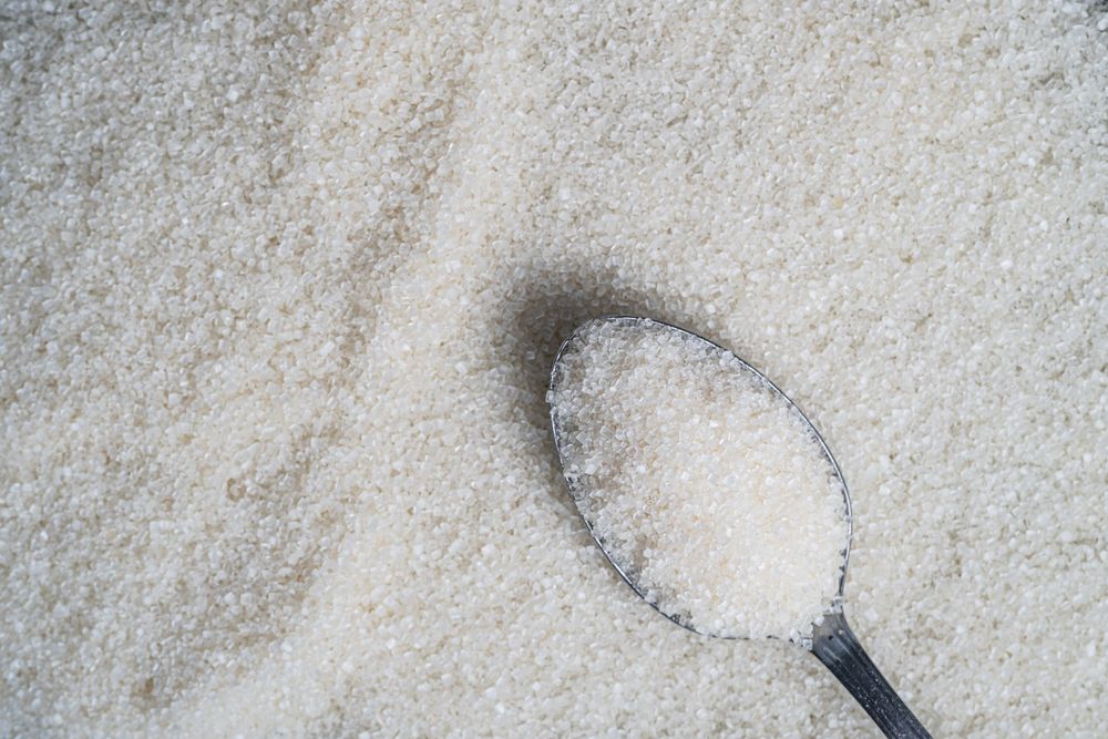Granulated sugar spread on a surface with a spoonful resting on top