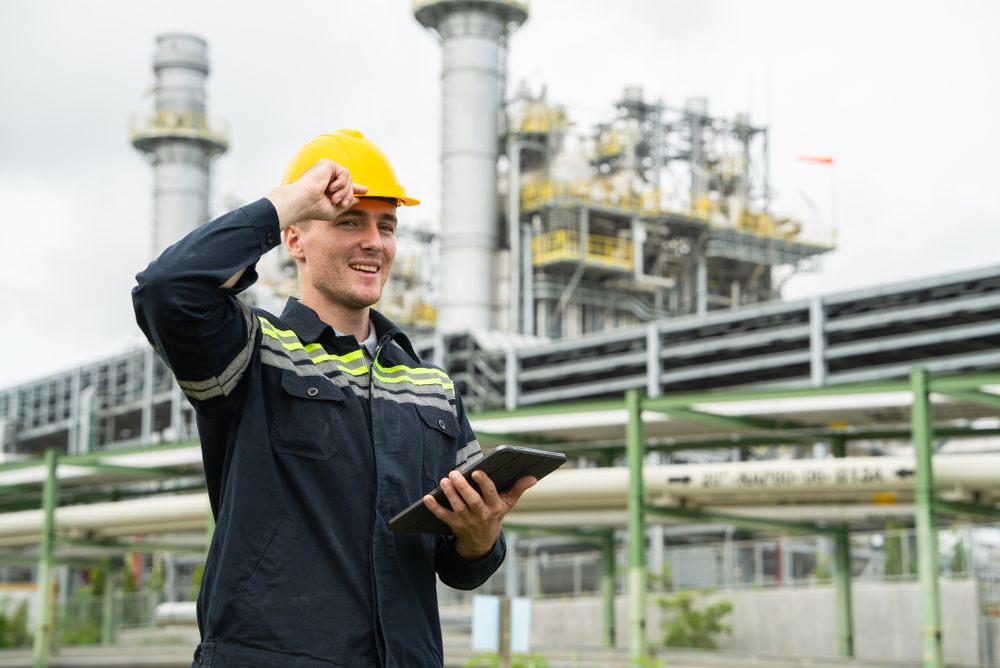 Refinery oil engineer worker in protection hardhat with digital tablet inspecting at petrochemical factory.