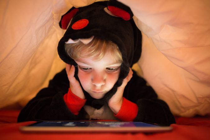 Boy using tablet under blanket
