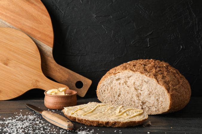 Cutting boards, bread, salt, knife and butter on wooden table against dark background, space for text
