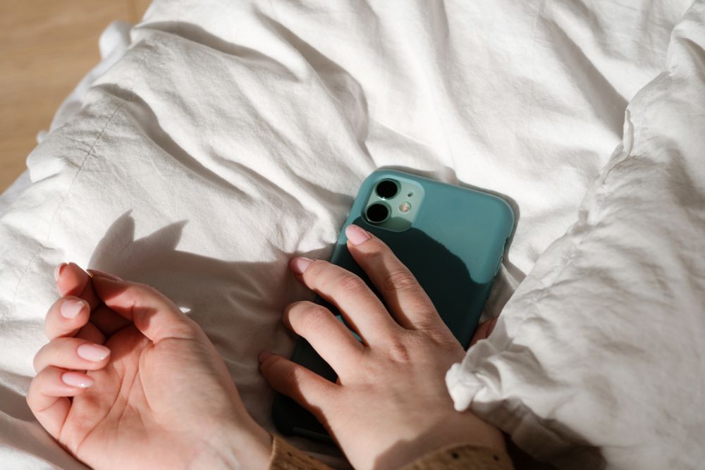 Hand holding smartphone on bed