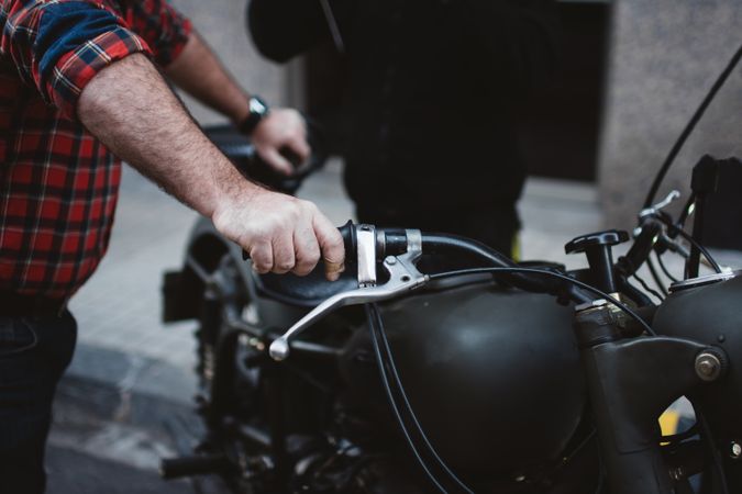 Crop man holding Motorbike on parking lot in town
