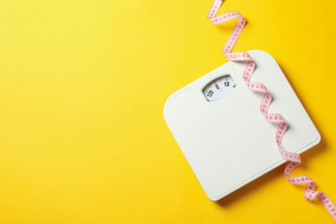 Scales and measuring tape on yellow background. Weight loss concept