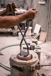 Man with lifting tongs taking metal ware from crucible
