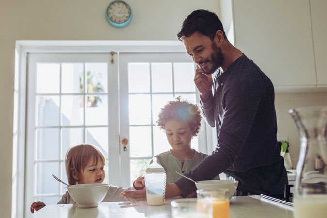 Man standing at the breakfast table talking over mobile phone with kids eating breakfast