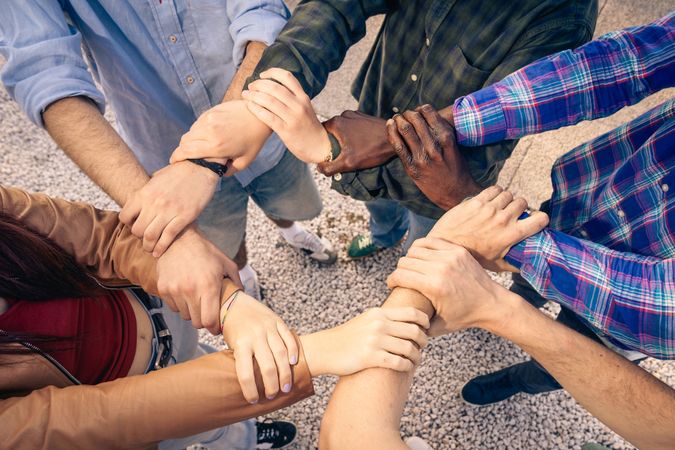 Diverse group of people linking arms together in a circle to show unity and teamwork.