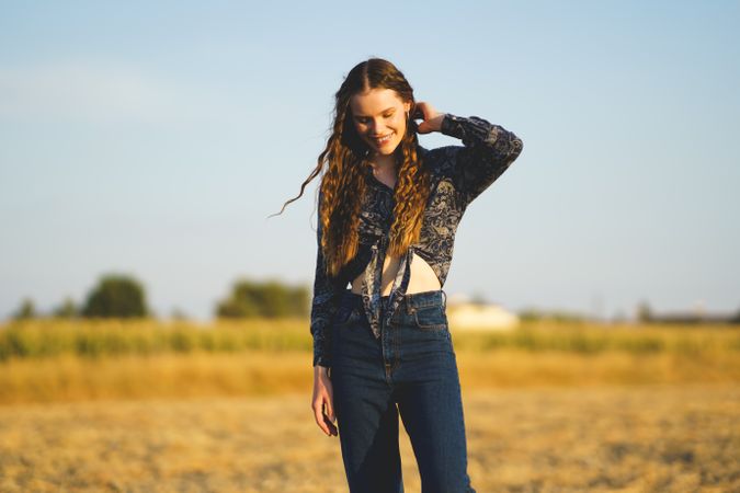 A young woman in a beautiful bohemian outfit poses gracefully in nature at sunset