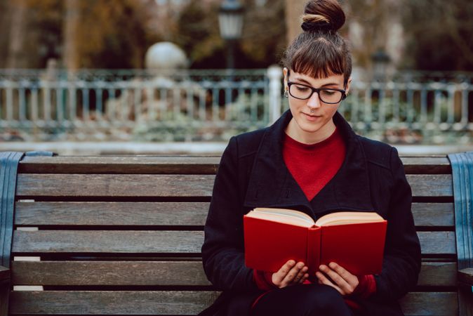 Young woman reading book on bench in park