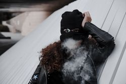 Woman in mask and jacket smoking on street