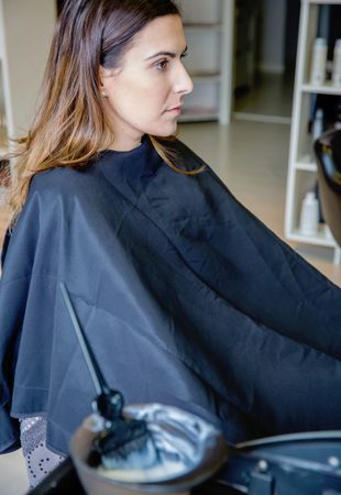 Woman sitting by bowl of hair dye in salon