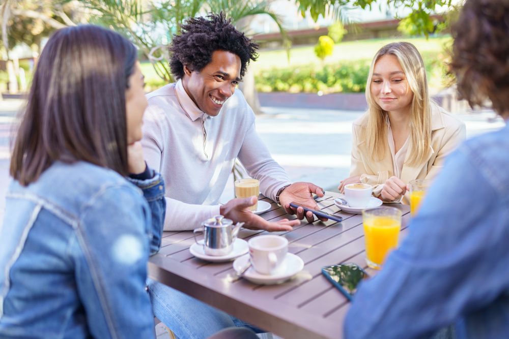 Multi-ethnic friends laughing over coffee and juice at outside table