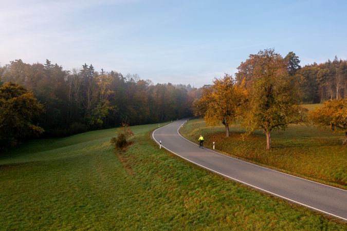 Winding road that leads toward the autumn forest, aerial view at sunrise