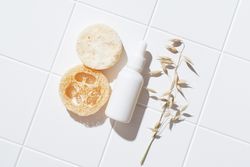 Loofah and bottle of serum arranged on bathroom floor