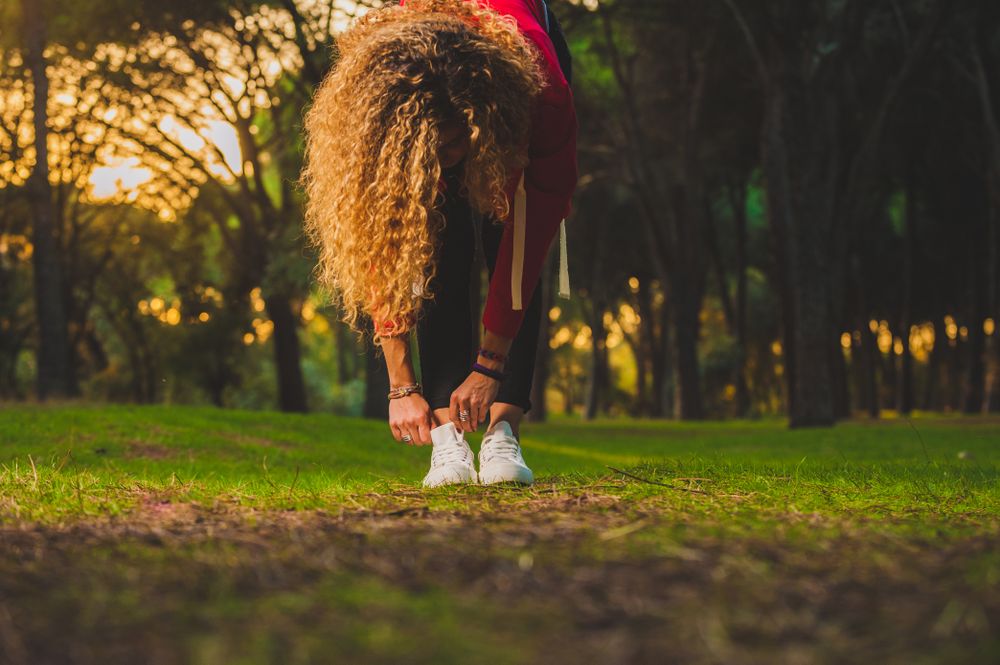 Sportive curly woman bending forward on lawn