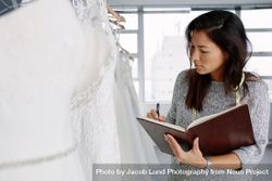 Female dressmaker working in bridal wear and writing in a diary 47KJk4