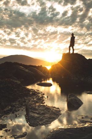 Silhouette of person standing on rock formation near body of water during sunset