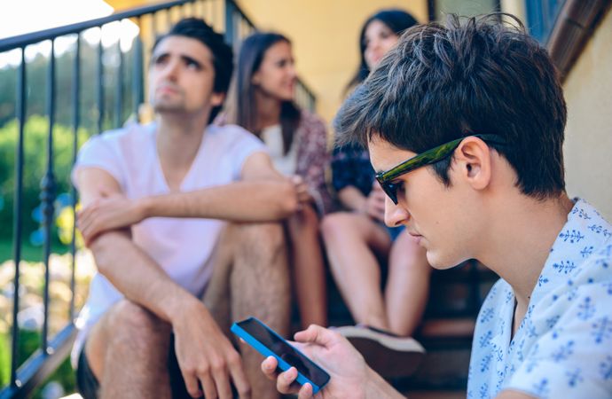 Young man looking a smartphone outdoors with his friends in background