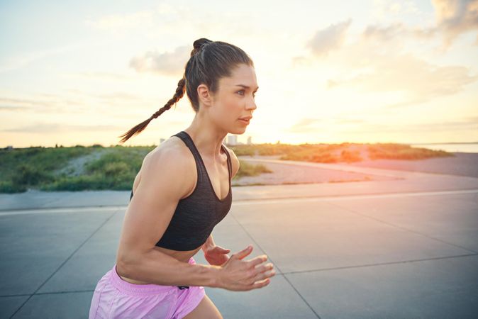 Intense athletic woman running with high pony tail in morning sun